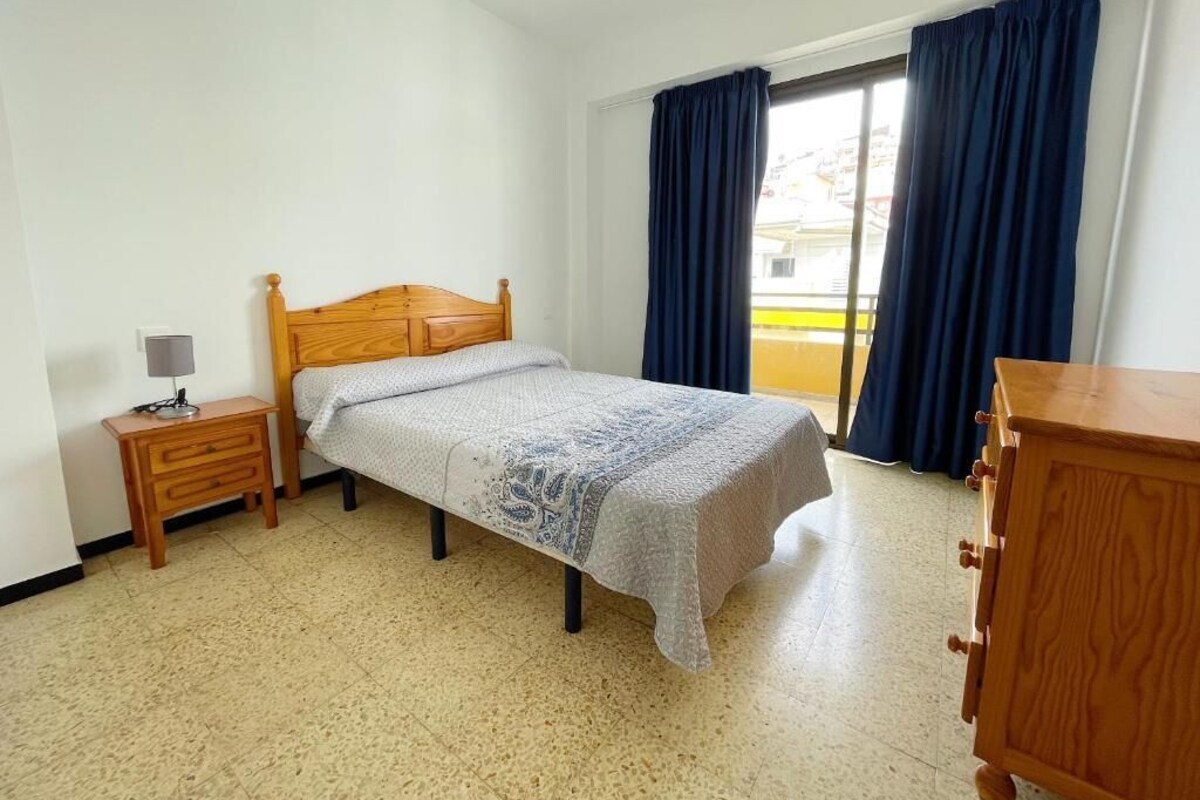 A bedroom with a wooden bed, a nightstand, a dresser, and a window with curtains.