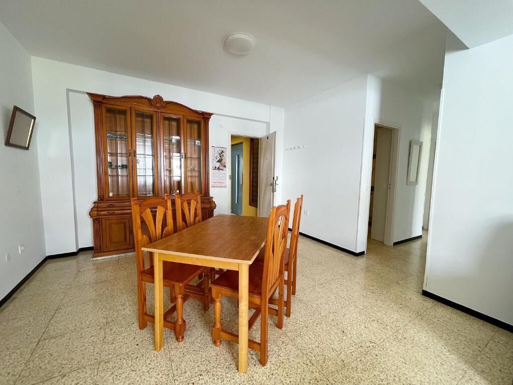 Un comedor con mesa y sillas de madera, un armario con puertas de cristal y suelo de baldosas.
