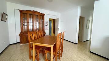 Un comedor con mesa y sillas de madera, un armario con puertas de cristal y suelo de baldosas.