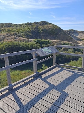Una pasarela de madera con un letrero, con vistas a un paisaje montañoso con vegetación.