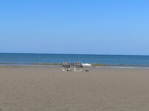 Una platja amb dues cadires de platja i un parell de sandàlies a la sorra.