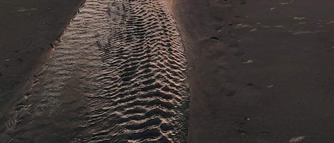 A beach with wet sand and a sunset in the background.