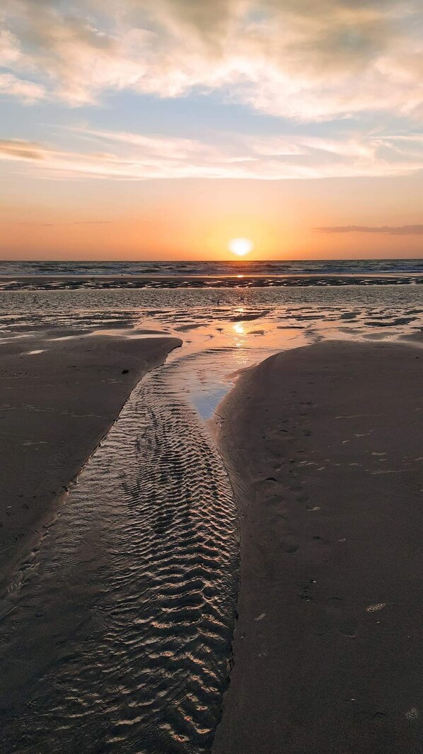 Una playa con arena mojada y un atardecer en el fondo.
