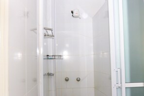 A shower with a glass door, a handheld showerhead, and a wall-mounted control panel.