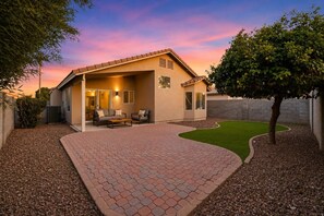 A house with a patio, outdoor seating, and a well-maintained lawn. - Spacious 3BR Home with Study & Large Backyard (Gilbert)