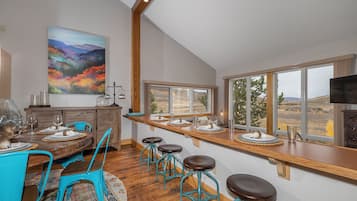 Un comedor con una mesa de madera, sillas azules y vistas al exterior a través de amplios ventanales.