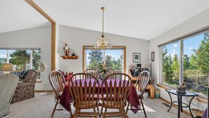 A dining area with a wooden table and chairs, a chandelier, and a view of trees through large windows.