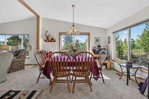 A dining area with a wooden table and chairs, a chandelier, and a view of trees through large windows.