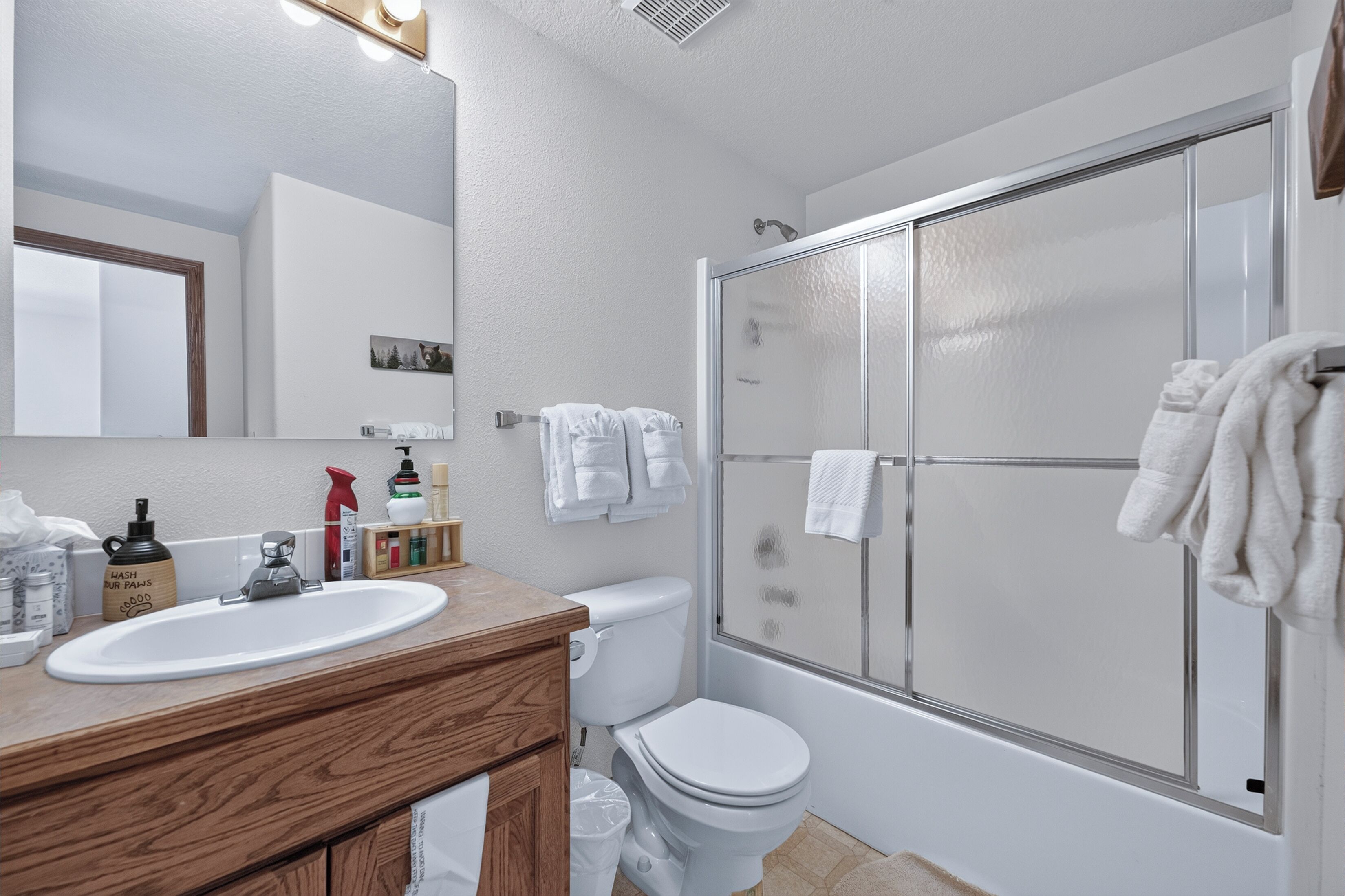 A bathroom with a wooden vanity, a white sink, a toilet, and a glass-enclosed shower.