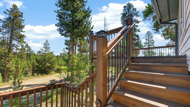 A wooden staircase leading to a deck with a railing, surrounded by trees and a clear sky.