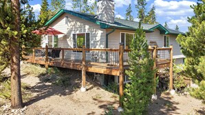 A cabin with a deck, surrounded by trees and a clear sky.