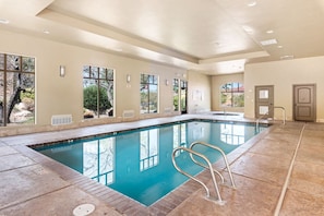 An indoor swimming pool with clear glass walls, a tiled floor, and a metal ladder. - Adventure Loft: Pool Views! Games! (Hurricane)