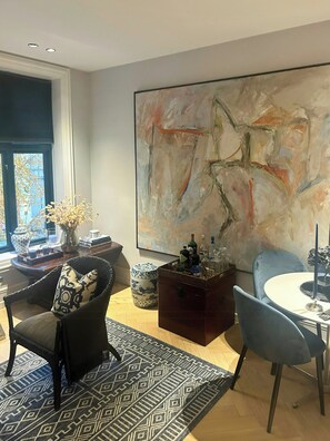 Ein modernes Wohnzimmer mit einem großen abstrakten Gemälde, einem Esstisch mit Stühlen und einer gemütlichen Sitzecke mit einem gemusterten Teppich.