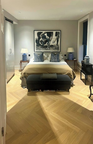 Ein Schlafzimmer mit einem Bett, Nachttischen, einer Lampe, einem Bild an der Wand und Holzboden.