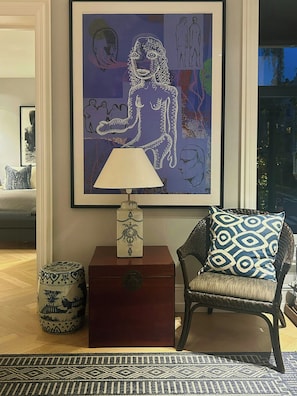 Ein Zimmer mit einem gerahmten abstrakten Gemälde, einer Lampe, einem gemusterten Sessel und einer dekorativen Vase.