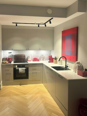 Eine moderne Küche mit Edelstahlgeräten, einem Fischgrätparkett und einem roten abstrakten Gemälde an der Wand.