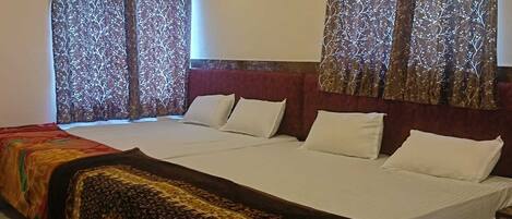 A hotel room with a large bed, two windows with patterned curtains, a ceiling fan, and an air conditioning unit.