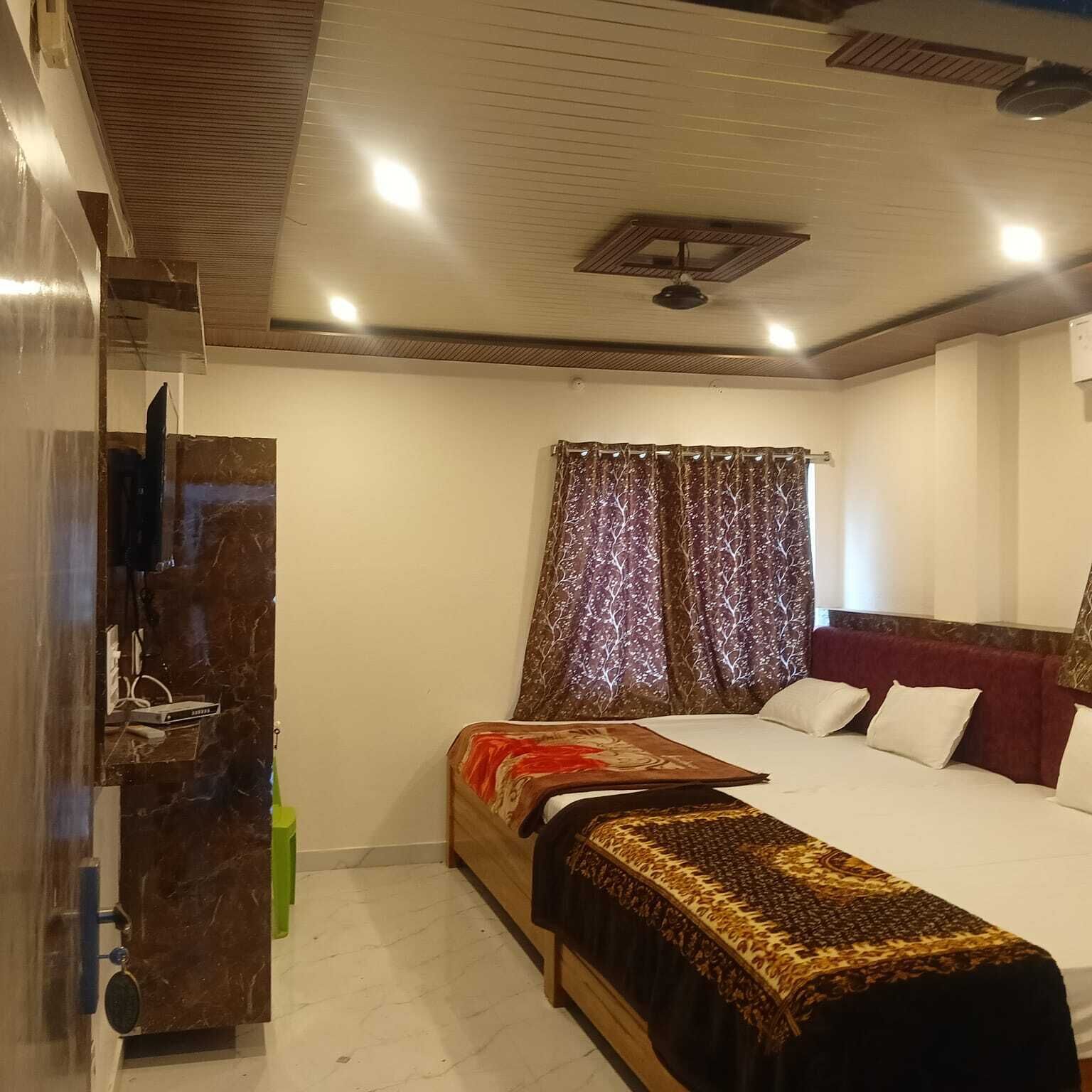 Une chambre à coucher avec un lit, une télévision, un ventilateur de plafond et une fenêtre avec des rideaux.