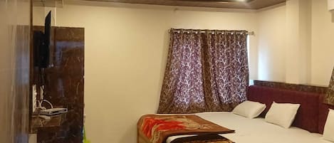 Un dormitorio con cama, televisor, ventilador de techo y ventana con cortinas.