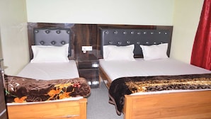 Une chambre d’hôtel avec deux lits en bois, chacun doté d’une tête de lit et de draps blancs. Une petite table de chevet en bois se trouve entre les deux lits.