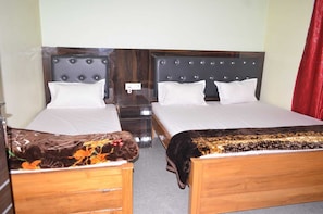 A hotel room with two wooden beds, each with a headboard and white bedding. There is a small wooden nightstand between the beds. - Hotel A.V. Priya (Rajgir)