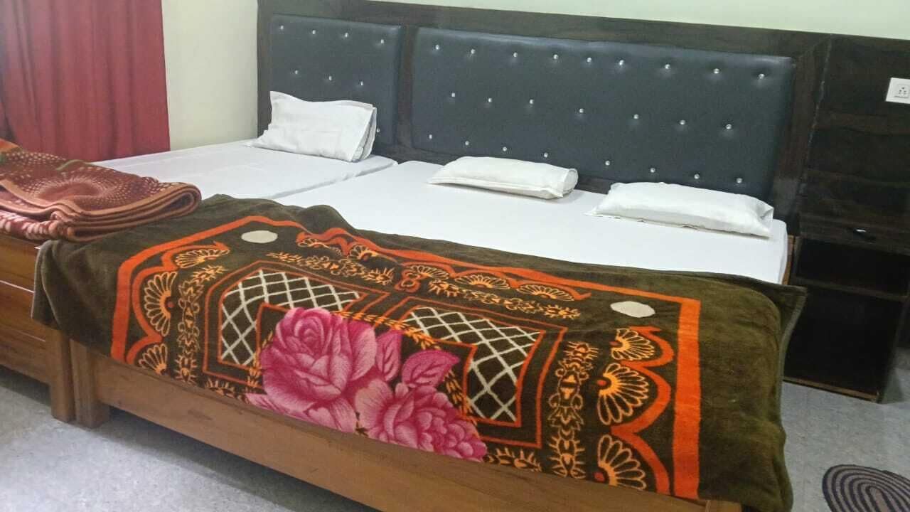 Uma cama de casal com colcha estampada e almofadas, uma cabeceira de madeira e uma televisão sobre um suporte.