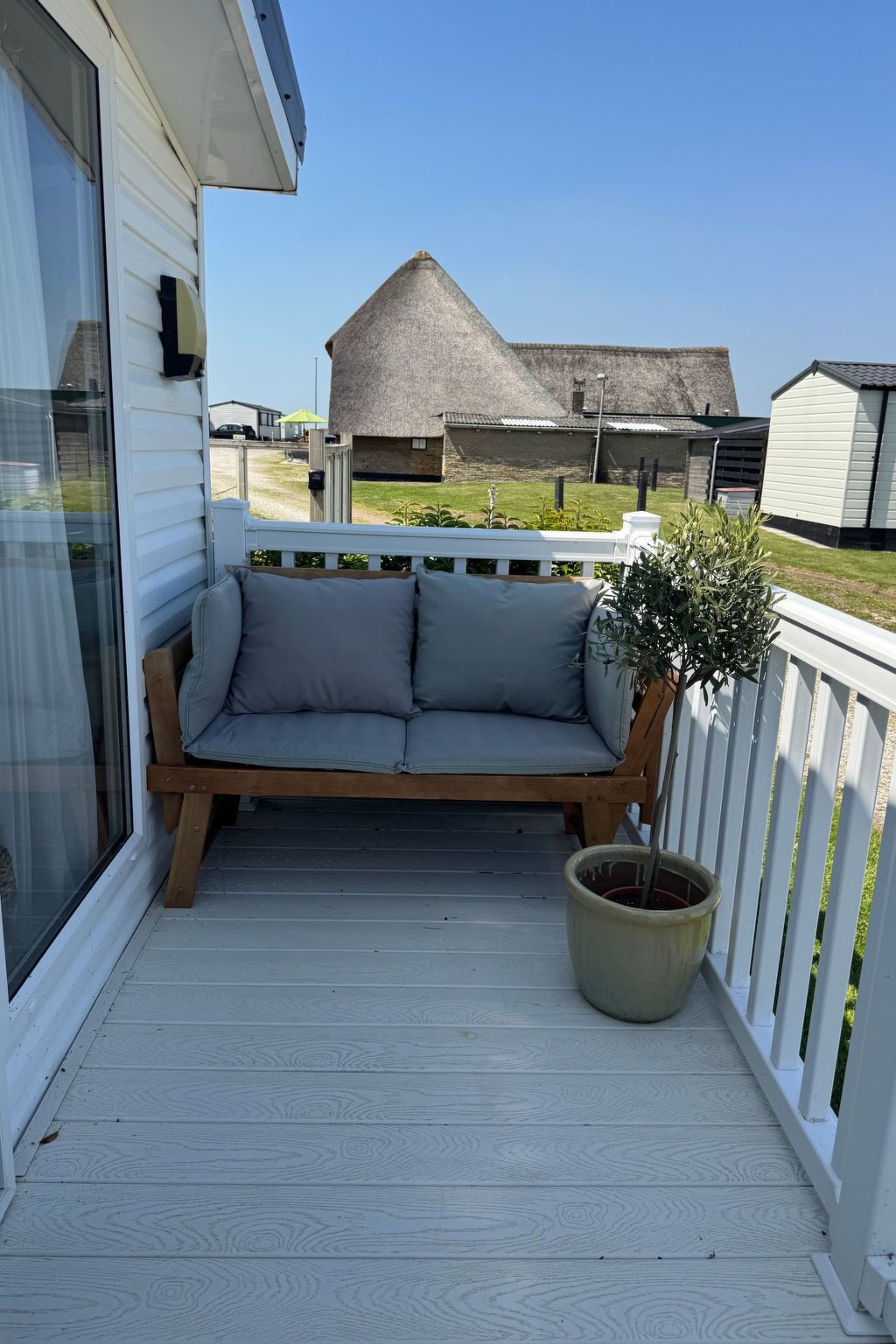 A covered outdoor seating area with a cushioned bench and a potted plant.