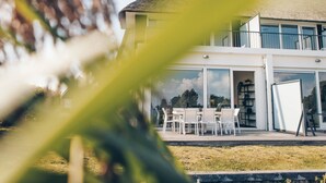 Una casa moderna de dues plantes amb un gran finestral de vidre que dona a una zona d'estar a l'aire lliure.