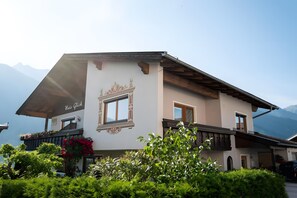 A traditional chalet with a balcony, a window with ornate trim, and a mountain backdrop.
