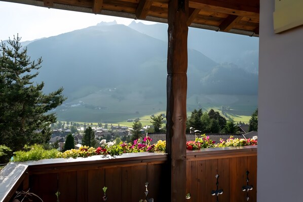 A wooden balcony with a view of a mountain range and a village below.
