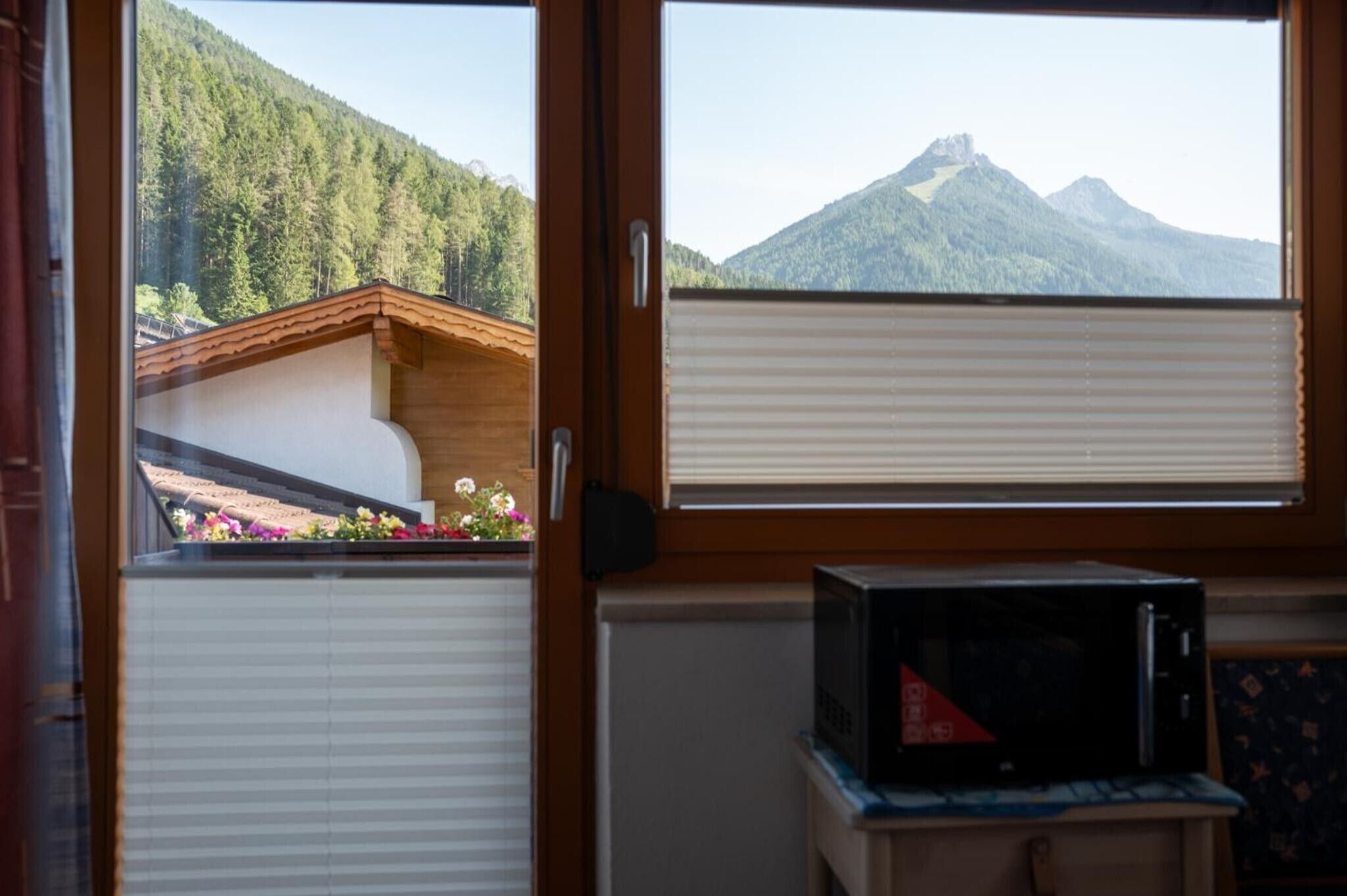 Ein Zimmer mit Blick auf einen Berg durch ein Fenster, eine Holztür und eine Mikrowelle auf einem kleinen Tisch.