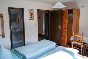 A bedroom with a bed, a wooden wardrobe, a bathroom with a mirror, and a hanging light fixture.