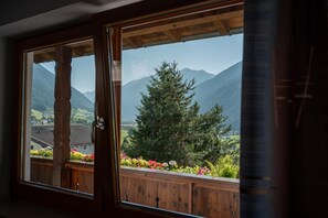 A wooden-framed window with a view of a mountainous landscape and a wooden deck with colorful flowers.