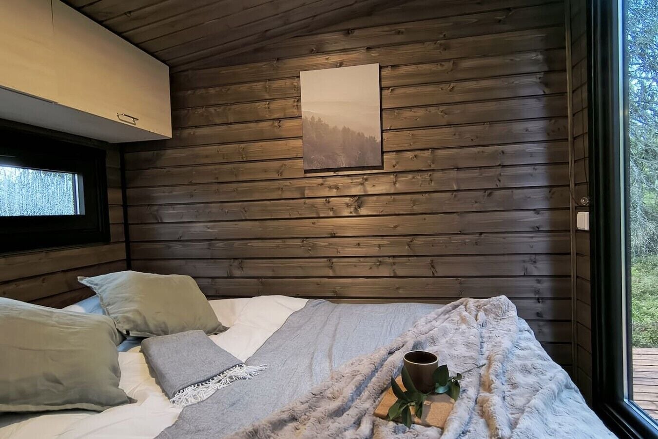 A bedroom with a bed, pillows, a blanket, a cup, and a plant.