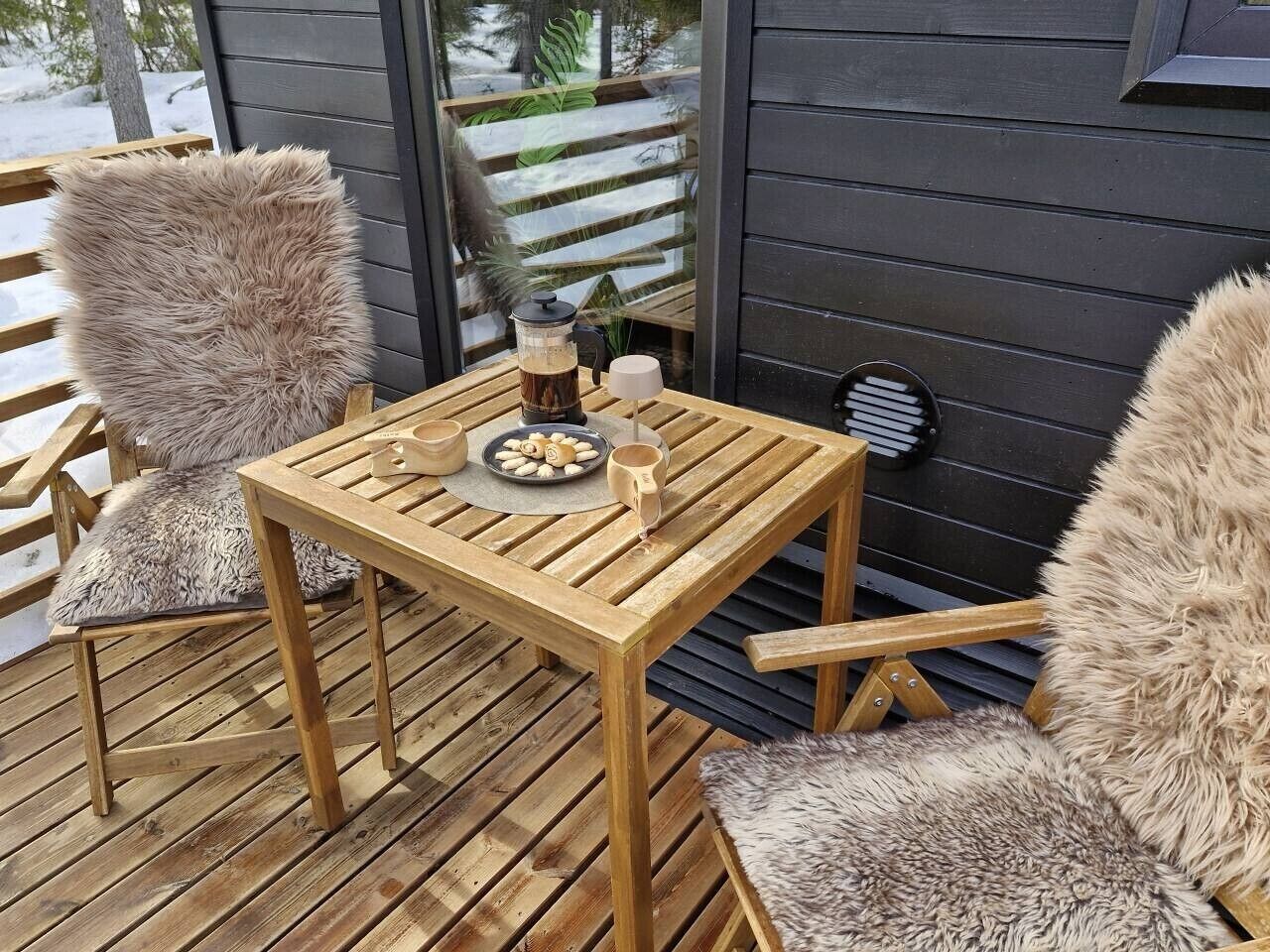A wooden deck with a table and chairs, a coffee maker, and a plate of cookies.