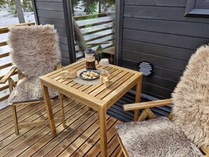 A wooden deck with a table and chairs, a coffee maker, and a plate of cookies.