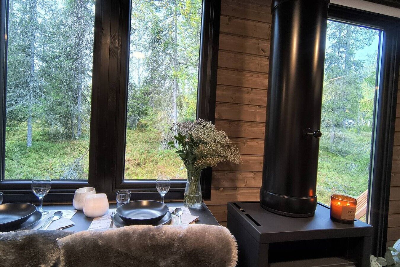 Una habitación acogedora con un ventanal grande, una estufa de leña y una mesa de comedor para dos.