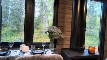 Una habitación acogedora con un ventanal grande, una estufa de leña y una mesa de comedor para dos.