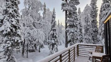 Un balcón cubierto de nieve con barandas de madera y una mesa con sillas.