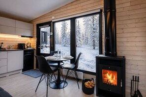 A modern kitchen with a large window, a dining table with chairs, and a wood-burning stove.