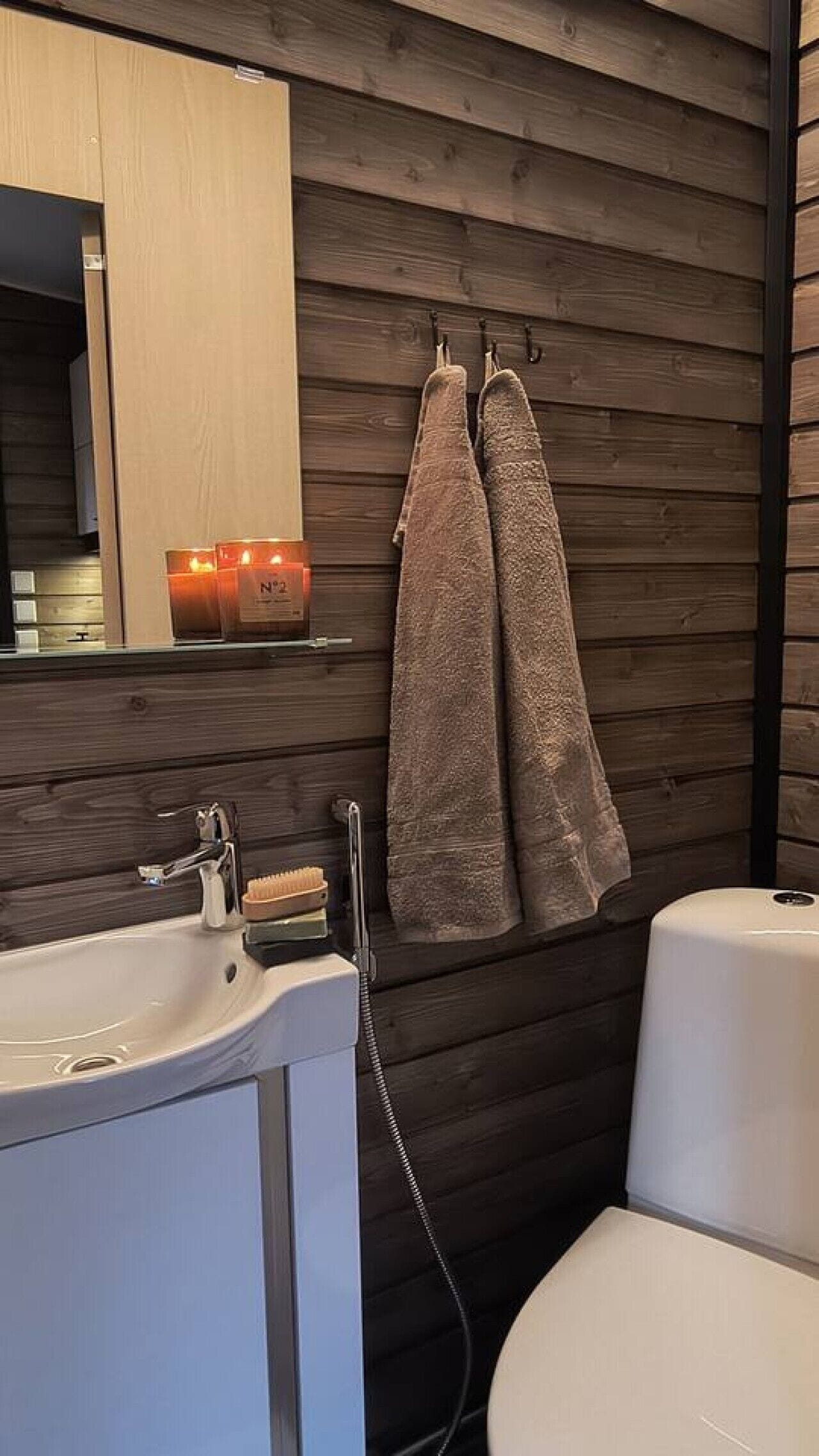 A bathroom with a wooden wall, a sink, a mirror, and a towel rack with two towels.