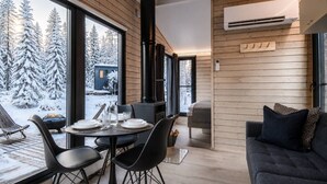 Un intérieur de chalet chaleureux avec un coin repas, un canapé et une vue sur une forêt enneigée.
