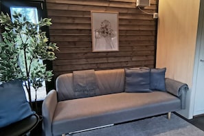 A modern living room with a grey sofa, a framed artwork on the wall, and a potted plant.