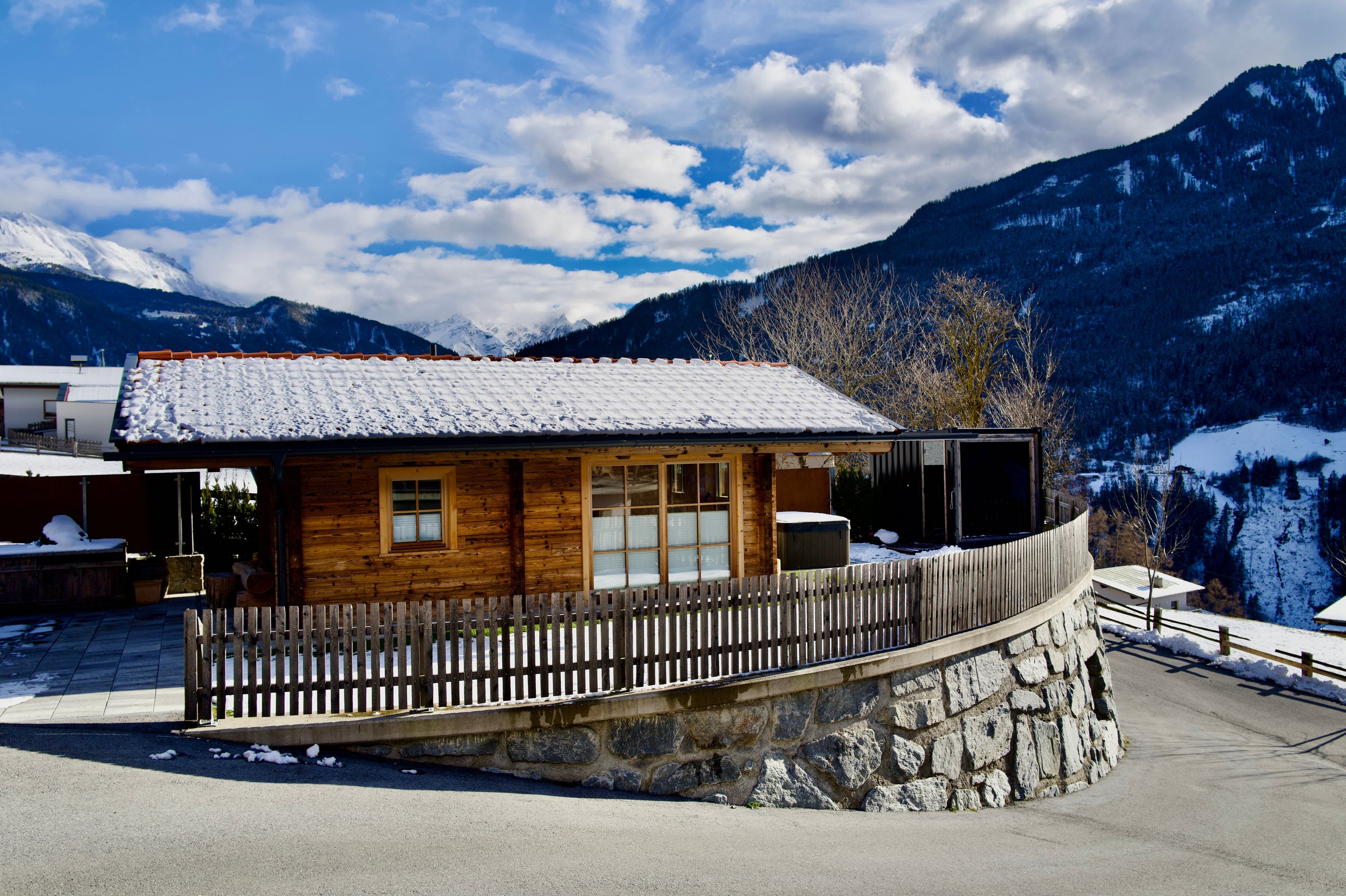 Eine Holzhütte mit schneebedecktem Dach, einer Steinsäule und einem Holzzaun.