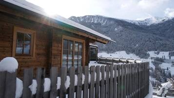 Uma cabana de madeira com grandes janelas, varanda e vista para montanhas cobertas de neve.
