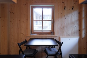 Una habitación con paneles de madera, una ventana, una mesa, dos sillas y un electrodoméstico blanco.