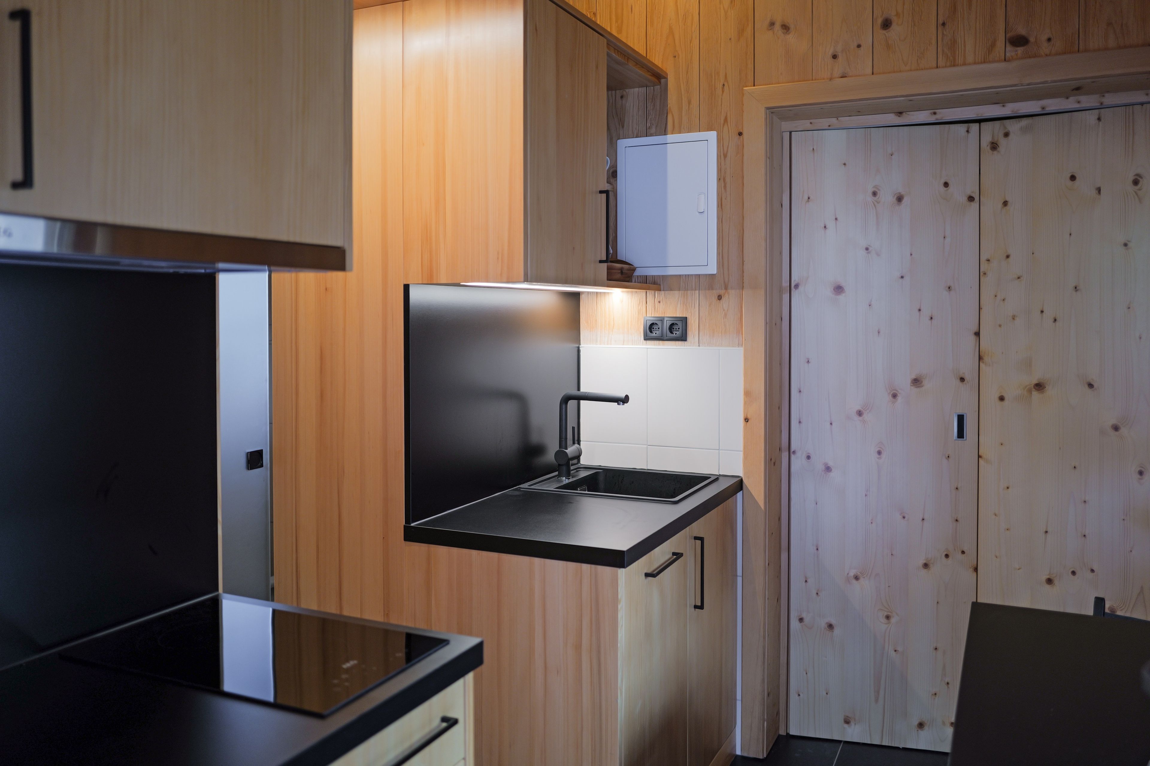 A compact kitchen with a black countertop, a sink, and wooden cabinetry.