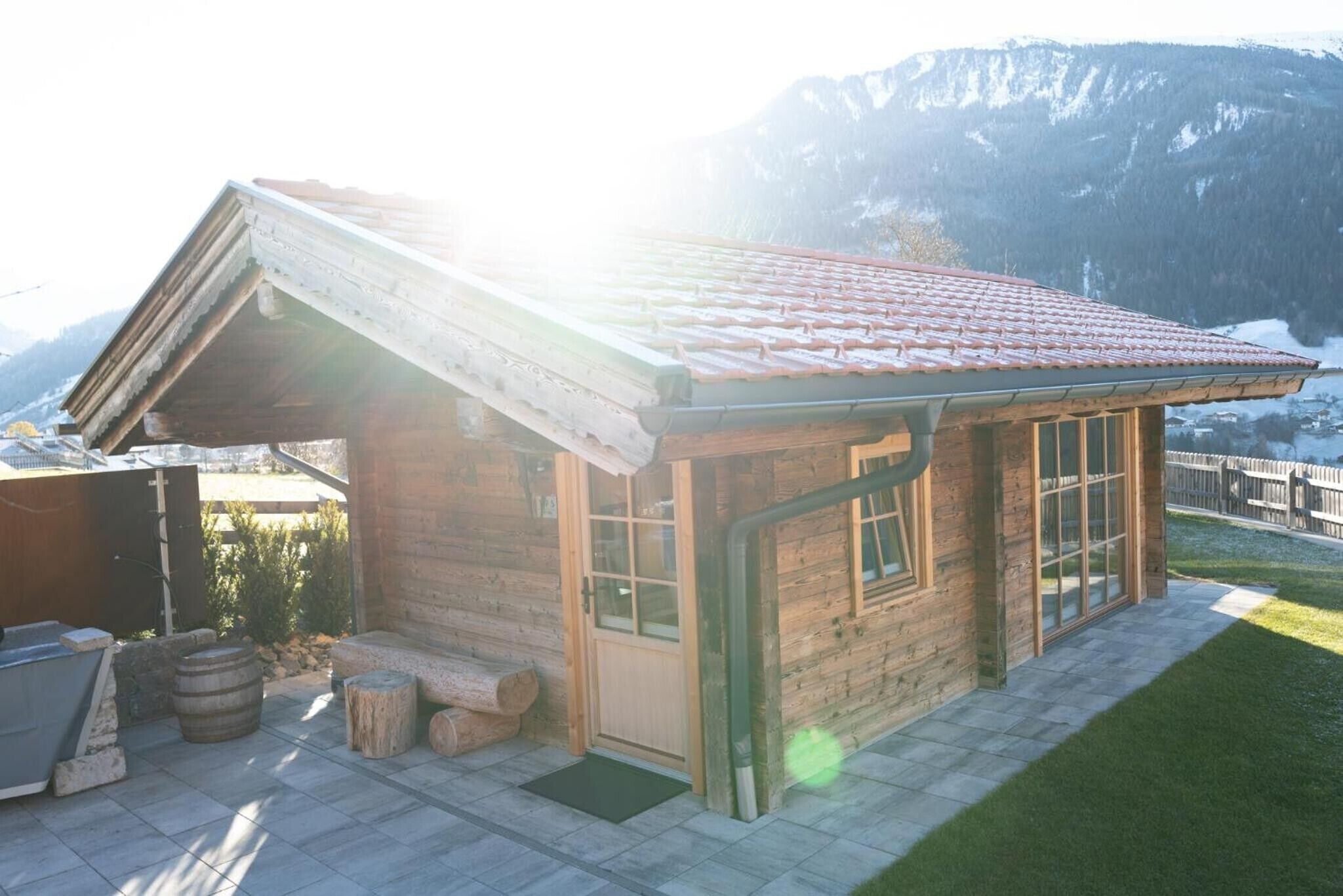Una cabaña de madera con techo de tejas, una puerta de cristal y un banco de piedra en el exterior.