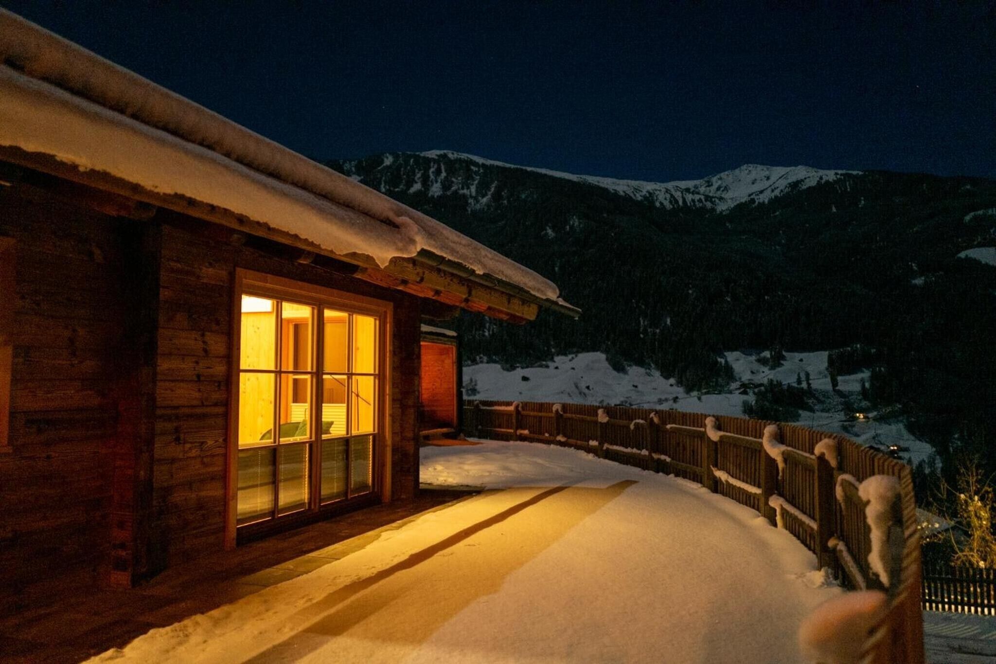 A wooden cabin with a snow-covered exterior, a glass door, and a wooden fence.