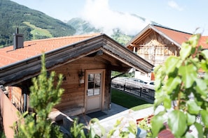 Een houten chalet met een rode dakbedekking, een houten deur en uitzicht op bergen op de achtergrond.